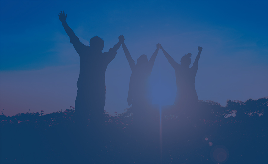 Three people holding hands and jumping outside.